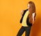 Ginger schoolgirl in black jacket, pants, yellow t-shirt. She is smiling, looking satisfied, posing on orange background. Close up
