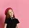 Ginger teenage girl in black dress, checkered shirt on waist, red hat and choker. She smiling, posing on pink background. Close up