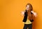 Ginger teenager in black jacket and pants, yellow t-shirt. She smiling, reaching for you, posing on orange background. Close up