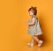 Ginger toddler female with two ponytails, in gray polka dot dress and white sandals. Smiling while posing on orange background