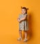 Ginger toddler female with two ponytails, in gray polka dot dress and white sandals. Smiling while posing on orange background