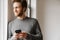 Ginger young man using mobile phone while leaning on wall