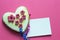 Gingerbread heart with white icing and pink flowers shit of paper on pink background. Love concept. Gift for womans and valentines