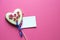 Gingerbread heart with white icing and pink flowers shit of paper on pink background. Love concept. Gift for womans and valentines