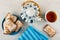 Gingerbread in sugar glaze in saucer, blue napkin, teapot, cup of tea on wooden table. Top view