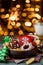 Gingerbreads in a brown wooden plate and a bottle of milk on a green wooden on the background of blurred garland
