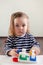 Girl 1,5 years old with long hair in a striped dress sits at the table and plays with a developing toy, Montessori technique