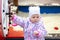 Girl 1 year walks on the playground, playing with children`s sports equipment. Baby jacket with flowers and a gray knitted hat fo