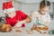 Girl 3 years old and boy 8 years old in Santa hat decorate gingerbread cookies with icing. Siblings in Christmas kitchen