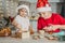 Girl 3 years old and boy 8 years old in Santa hat decorate gingerbread cookies with icing. Siblings in Christmas kitchen