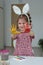 A girl of 4-5 years old in a pink dress, bunny ears cheerfully stands in a room with multicolored hands in watercolor