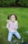 Girl of 6-7 years old in jeans sits on a green lawn and blows rainbow colored soap bubbles with interest