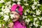 Girl of 8-9 years old in pink cap is hiding in flowering bushes.