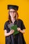 Girl in academic dress with diploma in her hands on a yellow background