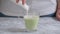 The girl is adding hot whipped milk to blended matcha tea in a glass cup.