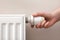 Girl adjusting heating radiator thermostat near white wall, closeup