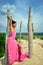 The girl of African belonging, with dreads on her head, in a pink dress, stands on a high hill leaning against a dry tree against