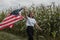 A girl with an American flag walks along a cornfield, labor Day,