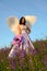 Girl with angel wings stands on a hillside and holds a large violet flower