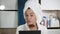 Girl aplying on face shine for skin. Attractive woman with towel and bathrobe on her head in bathroom applies