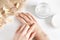 Girl applies moisturizer to her hands on a white background with dry flower petals and a piece of burlap  top view. Ecological