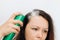 Girl applying dry shampoo spray on roots of dark fluffy hair.