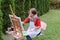 Girl artist paints picture and sits on chair at easel sides of t