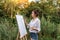 girl artist, woman paints picture landscape, summer forest, denim shorts creating creativity artistic mood. Blank white