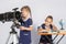 Girl astronomer looks through the eyepiece of the telescope, the other girl thinking waiting for the results of observations