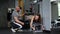 A girl athlete in gym under the guidance of man fitness instructor does exercises in machine. The trainer sits next to