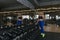 Girl of athletic physique poses near counter with dumbbells in gym. Fitness model dressed in sports leggings and top