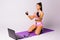 A girl with an athletic physique in a top and shorts stretches an elastic band in front of a laptop. Trainings online