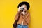 Girl in autumn clothes photographs on camera on a yellow isolated background, a tourist in a jacket and hat takes a photo