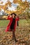 girl in autumn park standing under a strong wind, and holding her hat so it does not fly away