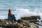 Girl in autumn windy weather sits by the sea on a rocky shore