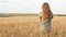 Girl back in dress standing among ears of corn in ripe golden wheat, young pretty woman enjoying rural landscape