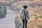 Girl with a backpack and a hat standing on a hill. River and forest below. Back view