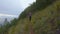 Girl with a backpack runs along the trail on a steep high slope of the sea coast