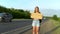 A girl with a backpack stands by the road and holds a sign with the inscription wherever you go. Hitchhiking. Stop the