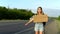 A girl with a backpack stands by the road and holds a sign with the inscription wherever you go. Hitchhiking. Stop the