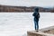 Girl with a backpack, young woman in a blue jacket and hood looks into the distance at frozen lake