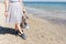 Girl with bag in hand standing on weat sand near sea. View of the legs in a lush gray skirt and sneakers