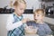 Girl baking cookie while brother tasting batter in kitchen