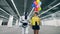 Girl with balloons and a droid walk in a room, holding hands.
