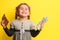 Girl with banknotes in hands on a yellow background, business child with world currency.