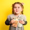 Girl with banknotes in hands on a yellow background, business child with world currency.