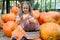 A girl with a basket of blooming heather sits among orange pumpkins. Autumn harvest