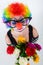 Girl in big black glasses and clown costume with a bouquet of flowers looks up