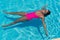 Girl in bikini relaxes relaxing, swimming in crystal clear water in swimming pool. Pretty girl in swimwear lies in