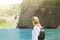 girl with a black backpack behind looking into the blue karst lake in the mountains
